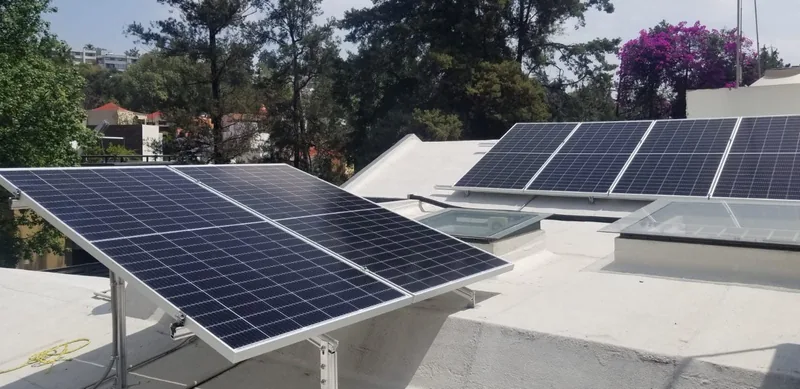 Paneles solares sobre una azotea blanca rodeada de árboles